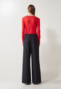 Haut rouge à manches longues associé à un pantalon noir à jambes larges. Le haut a une encolure ronde, tandis que le pantalon possède une taille élastique.