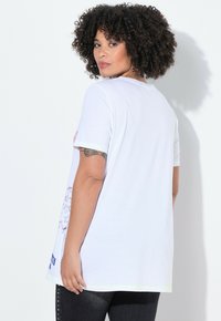 T-shirt en coton blanc avec des manches courtes, une coupe décontractée et des motifs d'étoiles multicolores sur les ourlets des manches et le bas sur le côté.