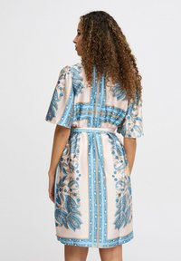 Rochie cu mâneci scurte, de culoare roz pal, cu modele florale albastre și margini decorative. Dispune de un cordon legat la talie.