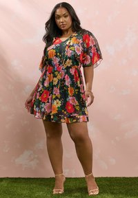 Lyhyt kukkamekko mustalla taustalla, jossa on eloisat punaiset, vaaleanpunaiset ja oranssit kukat, puffihihat ja rypytetty vyötärölinja.