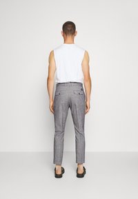 Gray tailored trousers with a slim fit, textured fabric, and multiple pockets, paired with a white sleeveless top. Black shoes worn.