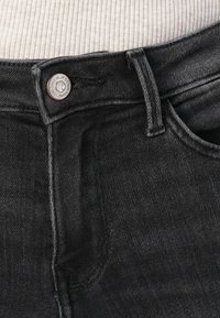 Black denim jeans featuring a high waist, silver button closure, and stitched detailing. Textured fabric with a classic, straight-leg design.
