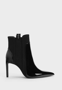 Botte noire à talon haut avec bout pointu, panneaux latéraux élastiques et finition brillante sur les sections avant et talon.