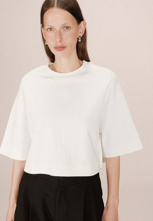 Top blanc court avec des manches courtes, col rond et une texture en coton lisse. Porté avec un pantalon noir taille haute.