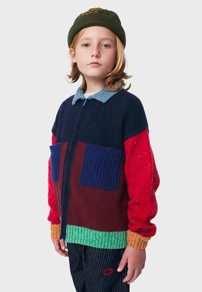 Strickjacke mit Reißverschluss in einem farbblockierten Design in Rot, Marineblau, Grün und Blau. Verfügt über zwei vordere Taschen und gerippte Bündchen.