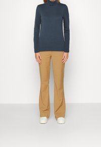 Marinblå långärmad polotröja tillsammans med ljusbruna utsvängda byxor, avslutat med vita sneakers. Slät tyg, figursydd design och avslappnad stil.