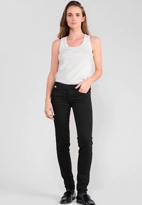Jeans noirs ajustés avec poches latérales et accessoires dorés, assortis à un débardeur blanc. Le tissu semble lisse avec une texture minimale.