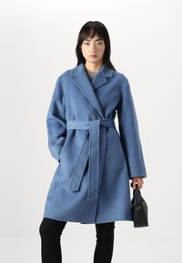 Abrigo de lana azul claro con cintura ceñida por un cinturón, solapas en pico y mangas largas, con una textura suave y dos bolsillos frontales.