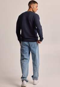 Navy textured sweater with a crew neck, paired with light blue loose-fit jeans and white sneakers, viewed from the back.