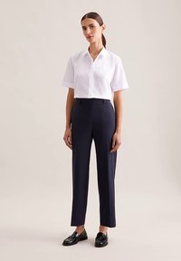 Weißes kurzärmeliges Hemd mit Kragen, kombiniert mit maßgeschneiderten dunkelblauen Hosen. Auffällige Details sind ein gerader Schnitt und elegante schwarze Loafers.