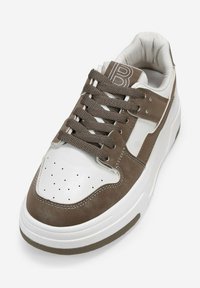 Sneaker marrone e bianco con tomaia in pelle testurizzata, punta perforata e lacci marroni. Suola bianca spessa con dettaglio in gomma antiscivolo.
