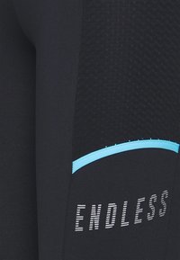 Czarne legginsy sportowe z teksturowanymi bocznymi panelami, jasnoniebieskimi akcentami oraz napisem "ENDLESS" wydrukowanym w wyraźnej, nowoczesnej typografii.