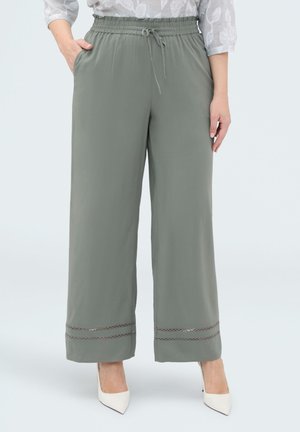 Donna che indossa pantaloni grigio chiaro a gamba larga con coulisse in vita e orlo decorativo abbinati a tacchi bianchi a punta e camicetta fantasia.