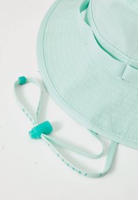 Sombrero de cubo en un verde menta claro con ala ancha, que presenta un tejido texturizado y una correa ajustable para el mentón, que se puede quitar, con un tope de plástico.