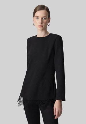 Black long-sleeve top with a straight cut, featuring a fringed hem and textured fringe detail at the bottom, made from soft fabric.