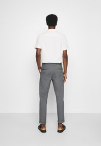 Chemise blanche à manches courtes et pantalon tailleur gris à coupe ajustée. Le matériau semble doux ; le pantalon présente deux poches arrière et des ourlets retournés.