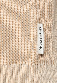 Stickad tröja med ett randigt mönster i beige och kräm, ribbad fåll och en klädesetikett med varumärket "Marc O'Polo."