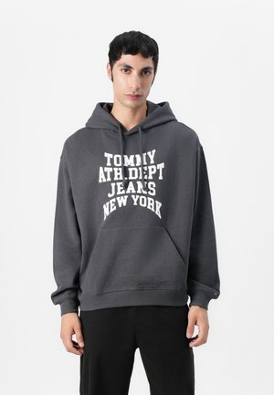 Grijze hoodie gemaakt van zachte stof, met een grote witte opdruk: "TOMMY ATH DEPT JEANS NEW YORK." Inclusief een voorzak en trekkoorden.