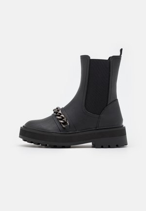 Black mid-calf leather boot with chunky sole, elastic side panel, rear pull tab, and decorative dark metal chain across the front.