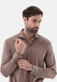 Braunes Langarmhemd aus glattem Stoff mit Knopfleiste, klassischen Kragen und dunklen Knöpfen an den Manschetten.