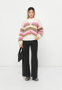 Gehaakte cardigan in beige, bruin en roze strepen, met een V-hals, vijf knopen en ballonmouwen, gecombineerd met wijde pantalon.