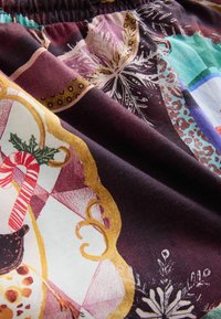 Mehrfarbiger Stoff mit komplizierten Mustern, der geometrische Formen, Zuckerstangen und florale Designs in reichen Lila-, Gold- und Weißtönen zeigt.