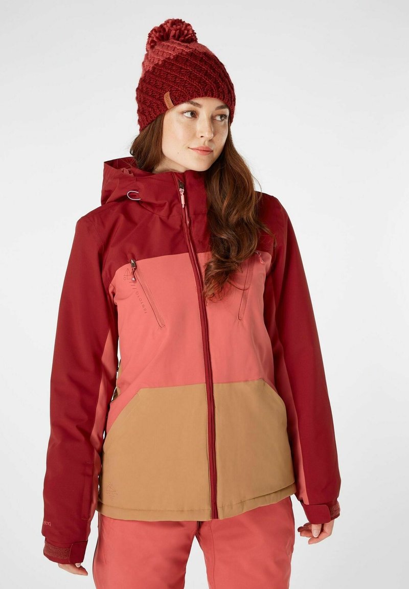 Rood en roze meerpaneel jas met een capuchon, voorzien van twee ritszakken. De gebreide muts heeft een pompon bovenop, benadrukt in een bijpassend kleurenschema.