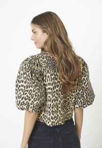Top corto in stampa leopardata con maniche a sbuffo; dettagli neri e tessuto testurizzato. Abbinato a jeans scuri a vita alta.