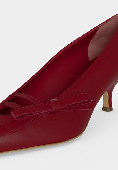Chaussure en cuir rouge à petit talon avec bout pointu et nœud décoratif à l'avant, vue de côté.