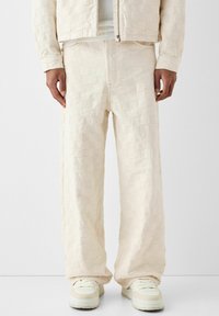 Krämfärgade överdimensionerade byxor med ett strukturerat rutmönster, med en dragkedja framtill, sidofickor och en avslappnad passform. Matchas med vita sneakers.