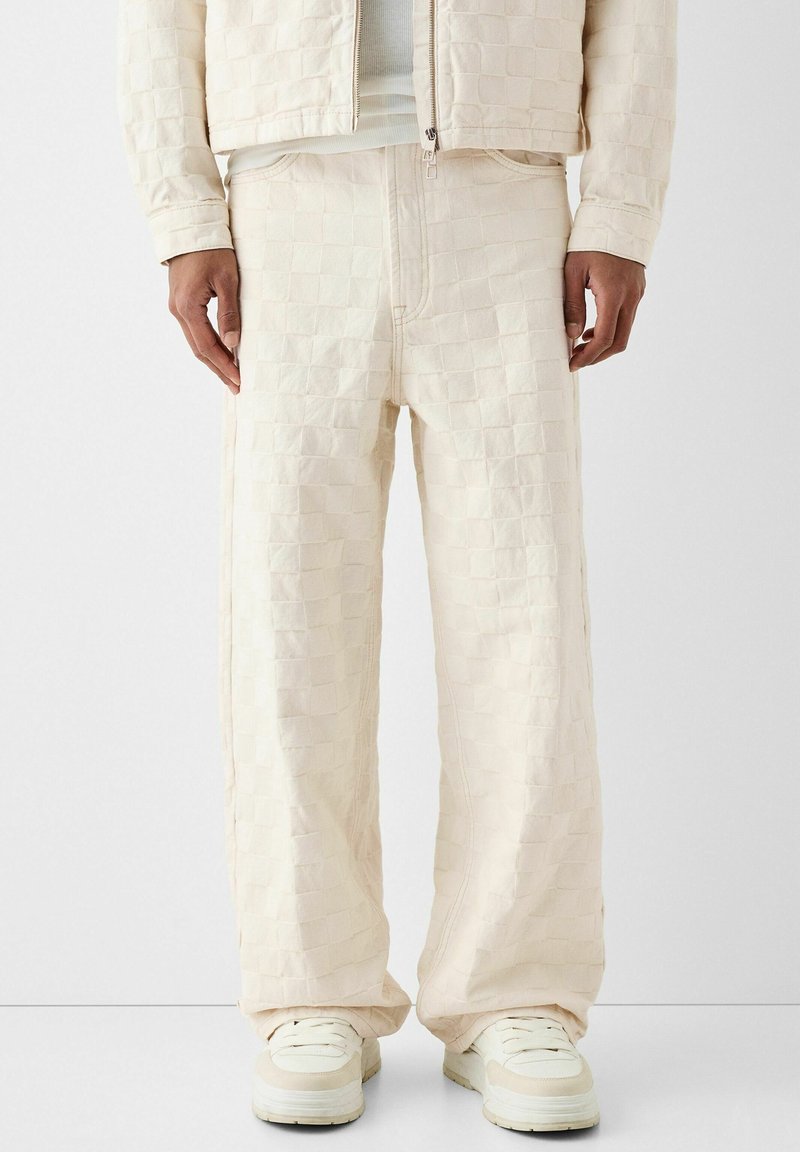 Krämfärgade överdimensionerade byxor med ett strukturerat rutmönster, med en dragkedja framtill, sidofickor och en avslappnad passform. Matchas med vita sneakers.
