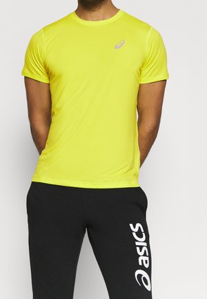 Homme portant un haut de sport à manches courtes jaune vif et un pantalon noir avec le logo blanc vertical "ASICS" sur la jambe droite.