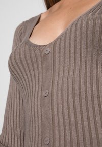 Ribbed brown cardigan with a V-neck, featuring three buttons and a textured pattern. The material appears soft and slightly stretchy.