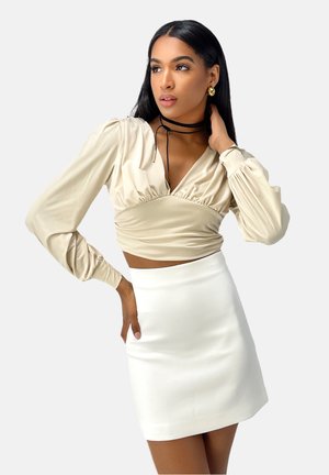 Haut beige en satin à manches longues avec un col en V et un détail froncé, assorti à une mini-jupe blanche. Texture lisse et coupe près du corps.