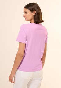 T-shirt à manches courtes en tissu coton lilas clair. Encolure ronde, coupe décontractée, avec une texture lisse et un design minimaliste.