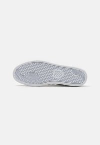 Hvit sneakersåle med et fiskebensmønster og en jevn, avrundet kant. Har en logo preget i midten av sålen.