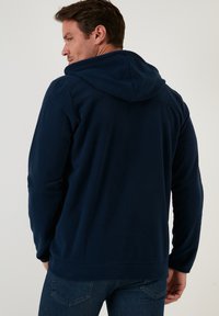 Felpa con cappuccio in pile blu navy con cordino, maniche lunghe, caratterizzata da una texture liscia e una vestibilità rilassata. Design semplice senza fantasie.