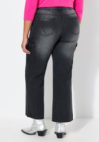 Pantaloni cargo in denim neri con gambe ampie, due tasche laterali e una texture sbiadita, abbinati a stivaletti argento. Vista posteriore mostrata.