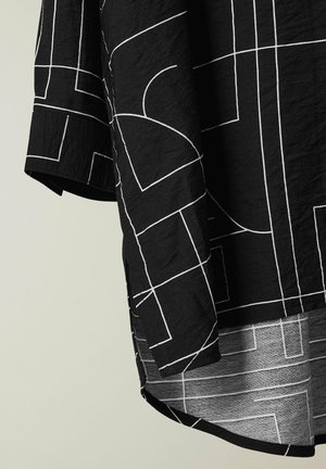 Tela negra con patrones geométricos de líneas blancas, mostrando la manga y el detalle del dobladillo curvado de una camisa.