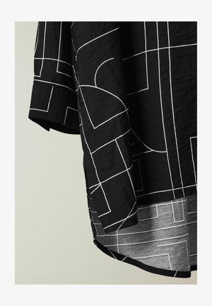 Tela negra con patrones geométricos de líneas blancas, mostrando la manga y el detalle del dobladillo curvado de una camisa.