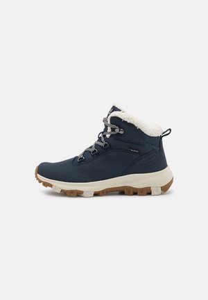 Scarpa da hiking blu navy con una tomaia in tessuto testurizzato, colletto in pelliccia sintetica e suola in gomma dotata di tacchetti aggressivi per una maggiore aderenza. Lacci neri e bianchi.