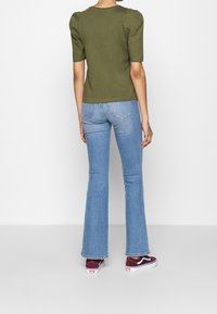 Oliven grøn kortærmet top med puffede skuldre parret med let blå flared jeans og bordeaux sneakers. Glat stof, tætsiddende design.