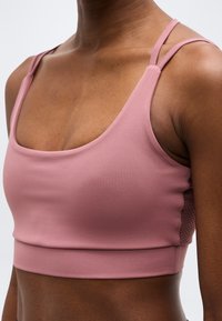 Κοντινό πλάνο ενός ατόμου που φοράει ροζ αθλητικό σουτιέν με διπλούς ιμάντες στους ώμους και λεπτομέρειες από δίχτυ στο πλάι.