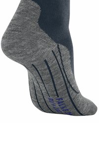 Zbliżenie szarej skarpetki z widocznymi teksturowanymi wzorami oraz ciemnoniebieską strefą pięty. Na podeszwie widoczne są niebieskie litery.