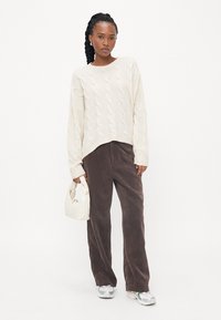 Kremasti džemper s pletenim uzorkom i opuštenim krojem; smešasti široki karirasti hlače; bela torba; svetlosive patike.