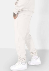 Beige sweatpants in een slim fit, met zijzakken en elastische manchetten, gecombineerd met witte sneakers voor een gecoördineerde uitstraling.