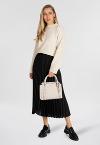 Beige gebreide trui, zwarte geplooide rok en opvallende zwarte platformlaarzen. De handtas is lichtroze met een patroonaccent en dubbele hengsels.