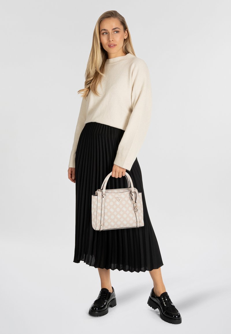 Beige gebreide trui, zwarte geplooide rok en opvallende zwarte platformlaarzen. De handtas is lichtroze met een patroonaccent en dubbele hengsels.