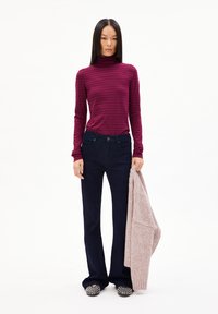 Maroon gestreifter Rollkragenpullover, dunkelblaue Jeans und ein hellrosaner Strickpullover in der Hand. Schwarze Schuhe mit silbernen Verzierungen.