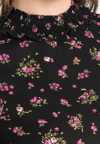 Blusa nera con motivo floreale caratterizzata da piccoli fiori rosa e foglie verdi. Collo arricciato con una texture smock. Tessuto morbido.